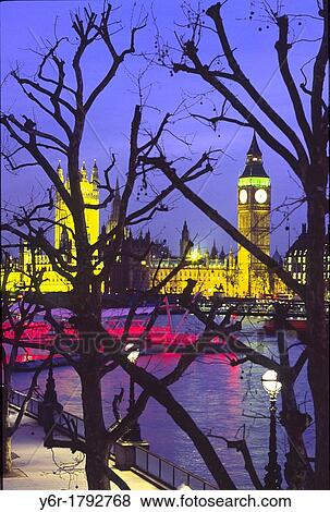 Stock Photo - View of an illuminated Big Ben and the Houses of Parliament across the River Thames at nightfall as seen from Hungerford Footbridge in London, England, during the blue hour. Fotosearch