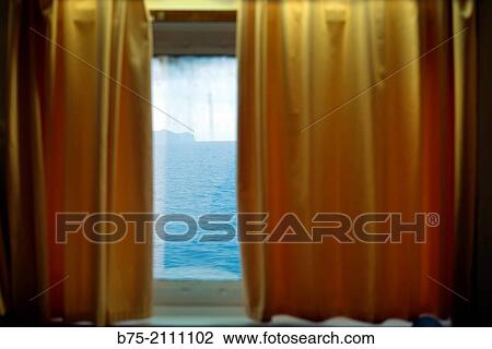 Stock Image - View of the sea and the sky through a window with yellow curtains, of a boat. Croosing the Mediterranean Sea from Ciutadella, Aberdeen to Alcudia, Mallorca, Balearic Islands, Spain. Fotosearch