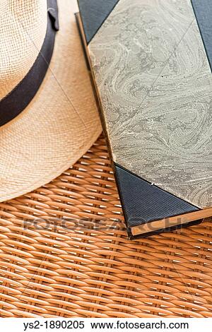 Stock Photography - Vintage book and classic straw hat lying on wicker chair. Fotosearch