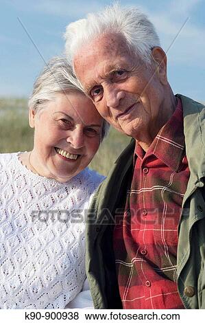 Waist up photograph of elderly caucasian couple looking into the camera, smiling and leaning to each other head to head with blue sky, Island of Amrum, Northfrisian, Schleswig_Holstein, Northern Germany, Europe View Large Photo Image Stock Photo - Waist up photograph of elderly caucasian couple looking into the camera, smiling and leaning to each other head to head with blue sky, Island of Amrum, Northfrisian, Schleswig_Holstein, Northern Germany, Europe. Fotosearch