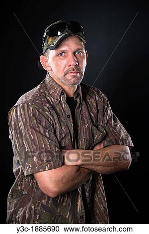 Stock Image - Waist up portrait of mature man in camouflage shirt and base cap, crossing arms, Male, 40 years, Caucasian. Fotosearch