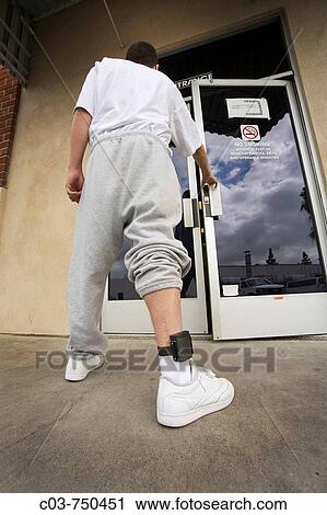Wearing an electronic monitoring device on his ankle, a teenage offender enters a county parole facility in Santa Ana, CA, USA View Large Photo Image Stock Image - Wearing an electronic monitoring device on his ankle, a teenage offender enters a county parole facility in Santa Ana, CA, USA. Fotosearch