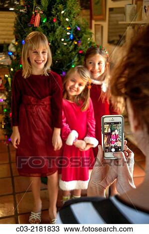 Wearing red holiday clothes, three sisters happily pose for their mother's cell phone camera in front of the family Christmas tree in Laguna Niguel, CA. View Large Photo Image Stock Image - Wearing red holiday clothes, three sisters happily pose for their mother's cell phone camera in front of the family Christmas tree in Laguna Niguel, CA.. Fotosearch
