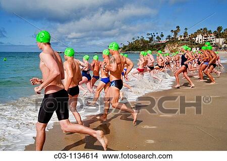 Wearing rubber caps with their classification numbers, teen applicants of both sexes for summer lifeguard jobs in Laguna Beach, California, race to the surf for their long-distance qualifying swim in cold 53-degree water Note city lifeguard station View Large Photo Image Picture - Wearing rubber caps with their classification numbers, teen applicants of both sexes for summer lifeguard jobs in Laguna Beach, California, race to the surf for their long-distance qualifying swim in cold 53-degree water Note city lifeguard station. Fotosearch