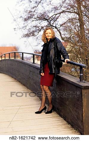 Well-dressed woman standing on wooden footbridge over a river and looks in the camera - Bavaria/Germany View Large Photo Image Stock Image - Well-dressed woman standing on wooden footbridge over a river and looks in the camera - Bavaria/Germany. Fotosearch