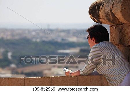 Stock Photo - White caucasian female with dark brown hair, wearing striped white top, age 32, views the landscape from the ramparts of the Citadel Citadella in Victoria Rabat, Gozo, Malta. Fotosearch