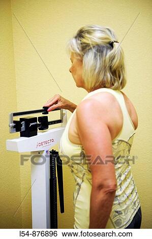Stock Photograph - White woman uses balance scale to measure weight. Fotosearch