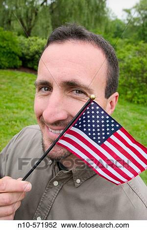 Wide-angle close-up of a young man, at a park, holding a small American flag by his face View Large Photo Image Stock Image - Wide-angle close-up of a young man, at a park, holding a small American flag by his face. Fotosearch
