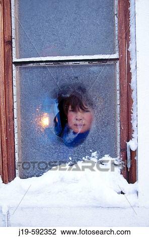 Stock Image - Winter, strong cold. Icy windows. 11 years old boy and a lantern.. Fotosearch