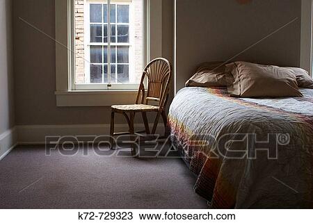 Stock Image - Without a person a bed and chair look lonely in the bedroom. Fotosearch