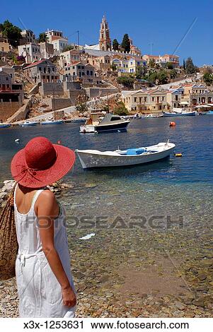 Stock Image - Woman admiring the view of the island town of Symi Greece. Fotosearch