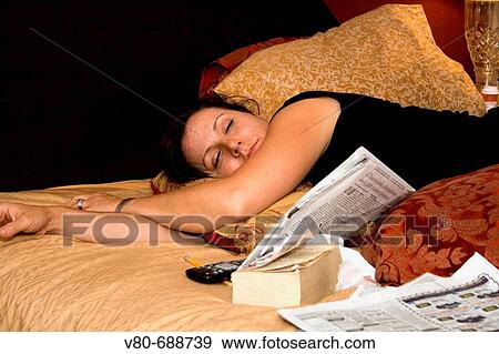 Woman age 38 resting on bed with newspaper, book and remote St Paul Minnesota USA View Large Photo Image Stock Photo - Woman age 38 resting on bed with newspaper, book and remote St Paul Minnesota USA. Fotosearch