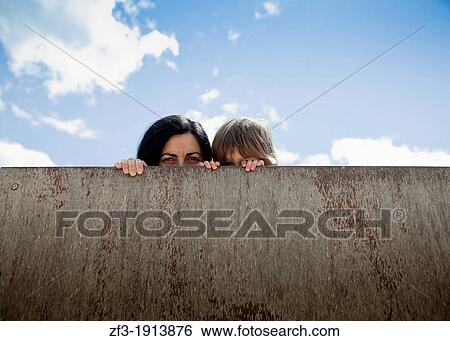 Woman and his son hiding behind a wall View Large Photo Image Stock Photograph - Woman and his son hiding behind a wall. Fotosearch