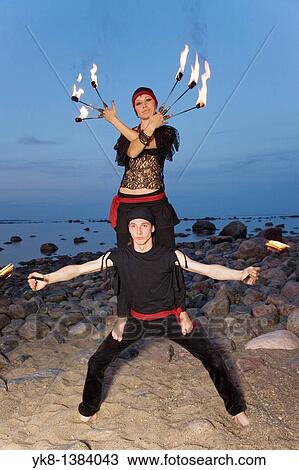 Stock Image - Woman and Man Fire Dancers in Costume Juggling Torches by Water. Fotosearch