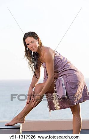 Woman applying lotion on legs in a terrace with the sea in background View Large Photo Image Stock Photograph - Woman applying lotion on legs in a terrace with the sea in background. Fotosearch