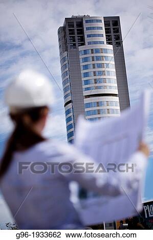 Stock Image - Woman architect with plans and helmet.. Fotosearch