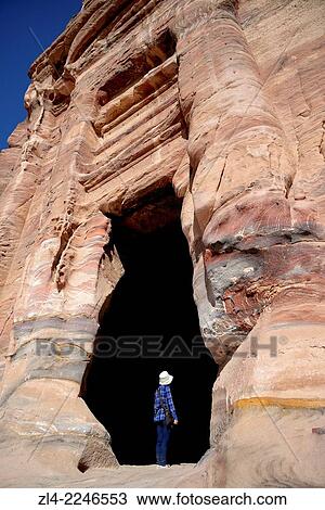 Stock Image - Woman at the entrance of a Royal Tomb carved in the mountain. Jordan (Hashemite Kingdom of), Ma'an Governorate (Maan), ancient city of Petra. Model Released.. Fotosearch