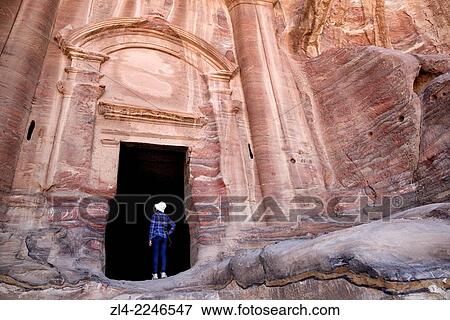 Stock Photo - Woman at the entrance of the Renaissance Tomb carved in the mountain. Jordan (Hashemite Kingdom of), Ma'an Governorate (Maan), ancient city of Petra. Model Released.. Fotosearch