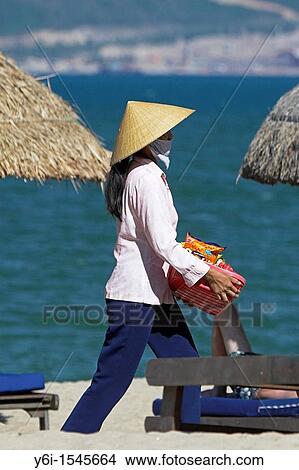Woman beach vendor in conical hat walks between woven beach umbrellas Nha Trang south east Vietnam View Large Photo Image Picture - Woman beach vendor in conical hat walks between woven beach umbrellas Nha Trang south east Vietnam. Fotosearch