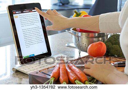 Stock Image - Woman browsing cooking instruction online with Epicurious iPad cooking app. Fotosearch