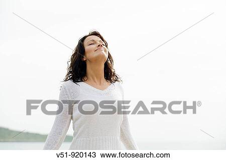 Stock Image - woman by the sea breathing fresh air. Fotosearch