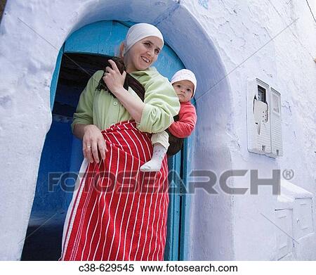 Stock Photography - Woman carrying her baby in the streets of Chefchaouen, Morocco, Africa. Fotosearch