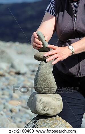 Woman carrying out the art of stone balancing on a deserted beach. View Large Photo Image Stock Image - Woman carrying out the art of stone balancing on a deserted beach.. Fotosearch