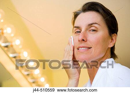 Stock Photo - Woman cleaning face with cotton pad in the bathroom. Fotosearch