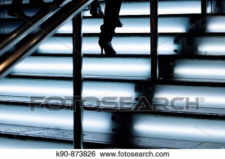 Stock Photograph - Woman climbing up neon lit stairs where her shoes are only seen as a silhouette, Hong Kong, China, Asia. Fotosearch