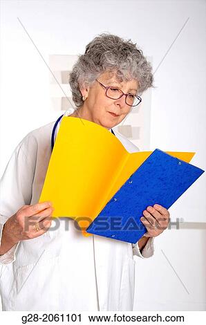 Woman doctor, in a white overall, senior woman with grey hair, red glasses and stethoscope around her neck, holding and looking at medical files in her hand, in hospital or clinic View Large Photo Image Stock Image - Woman doctor, in a white overall, senior woman with grey hair, red glasses and stethoscope around her neck, holding and looking at medical files in her hand, in hospital or clinic. Fotosearch