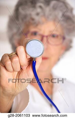 Woman doctor, in a white overall, senior woman with grey hair, red glasses and stethoscope in front of her, facing and looking at patient, in front of her, in hospital or clinic View Large Photo Image Stock Image - Woman doctor, in a white overall, senior woman with grey hair, red glasses and stethoscope in front of her, facing and looking at patient, in front of her, in hospital or clinic. Fotosearch