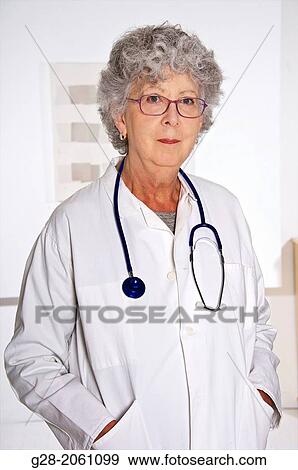 Stock Photo - Woman doctor, in a white overall, senior woman with grey hair, red glasses and stethoscope around her neck, in hospital or clinic. Fotosearch