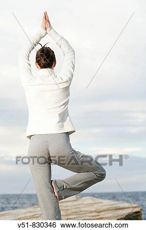 Stock Photograph - Woman doing yoga in a cliff by the sea. Fotosearch