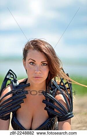 Stock Image - Woman dressed up with a futuristic space look costume holding a rusty trident, creating a modern interpretation of Salacia, Neptune's queen, an ocean Roman deity.. Fotosearch