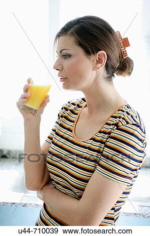 Stock Photo - Woman drinking a healthy natural orange juice on the kitchen. Fotosearch