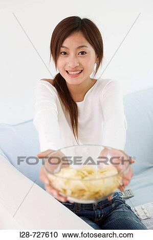 Stock Image - Woman eating chips on sofa. Fotosearch