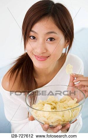 Stock Image - Woman eating chips on sofa. Fotosearch