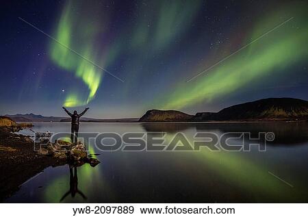Stock Photo - Woman enjoying the view of the Northern Lights, at Lake Thingvellir, Iceland. Thingvellir National Park is a UNESCO World Heritage Site.. Fotosearch