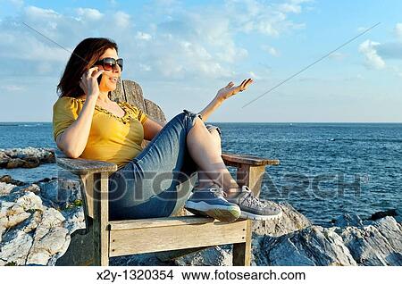 Woman enjoys the coastal view while speaking on a mobile phone View Large Photo Image Picture - Woman enjoys the coastal view while speaking on a mobile phone. Fotosearch