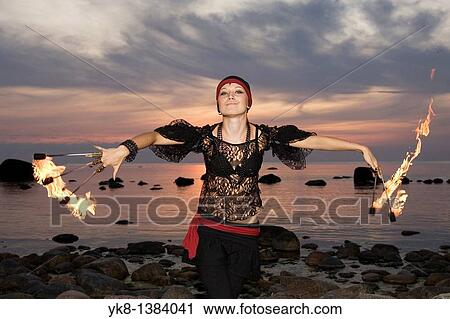 Stock Image - Woman Fire Dancer Juggling Torches by Water. Fotosearch