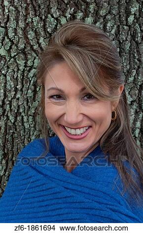 Woman from Eastern Europe portrait against tree in park with blue shawl smiling View Large Photo Image Picture - Woman from Eastern Europe portrait against tree in park with blue shawl smiling. Fotosearch
