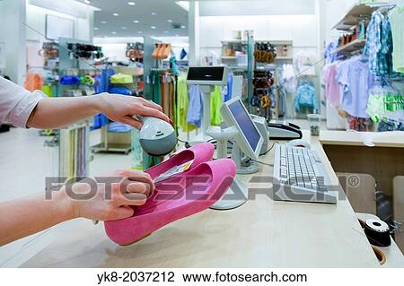 Stock Image - Woman hands holding price scanner. Fashion clothing store. Cashier register, computer on sales counter in shop. Shoes, pricing, shopping.. Fotosearch