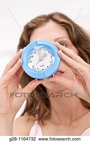 woman holding a blue alarm clock in front of her face View Large Photo Image Stock Image - woman holding a blue alarm clock in front of her face. Fotosearch