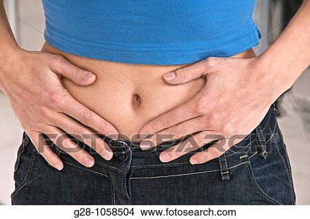 Picture - woman holding her stomach and suffering, periods or stomach pains, head invisible. Fotosearch