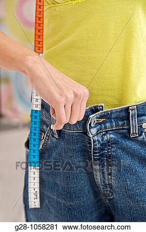 woman holding her too tight or too large jeans, dieting, with a measuring tape hanging from her neckclose up View Large Photo Image Stock Image - woman holding her too tight or too large jeans, dieting, with a measuring tape hanging from her neckclose up. Fotosearch
