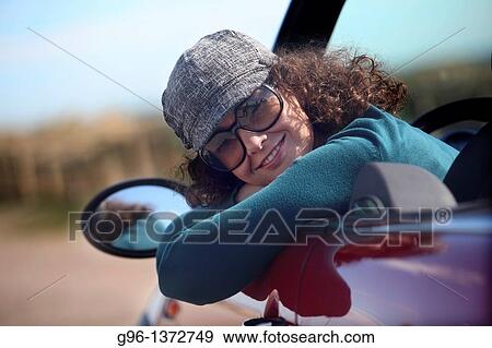 Stock Photo - woman in a convertible relaxing at the beach. Fotosearch