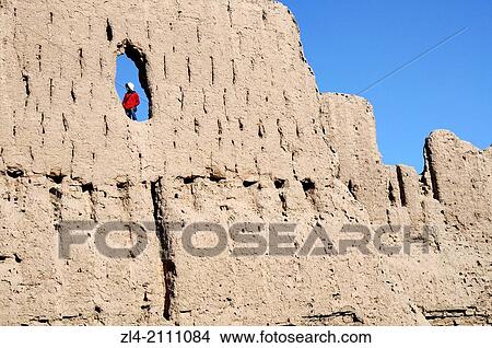 Picture - Woman in a hole in a wall of Qyzyl Qala desert fortress. Uzbekistan, Karakalpakstan. Model Released.. Fotosearch