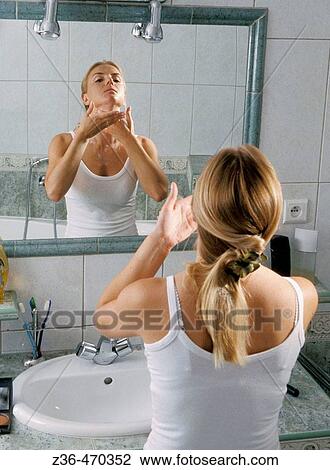 Stock Image - woman in bathroom putting cream. Fotosearch