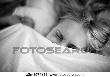 Stock Image - Woman in bed under covers cringing. Fotosearch