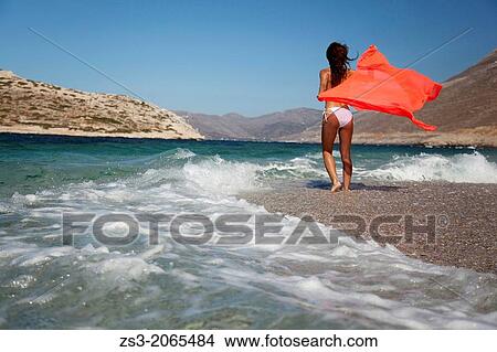 Picture - Woman in bikini walking towards the waves at the beach, Amorgos, Cyclades Islands, Greek Islands, Greece, Europe.. Fotosearch